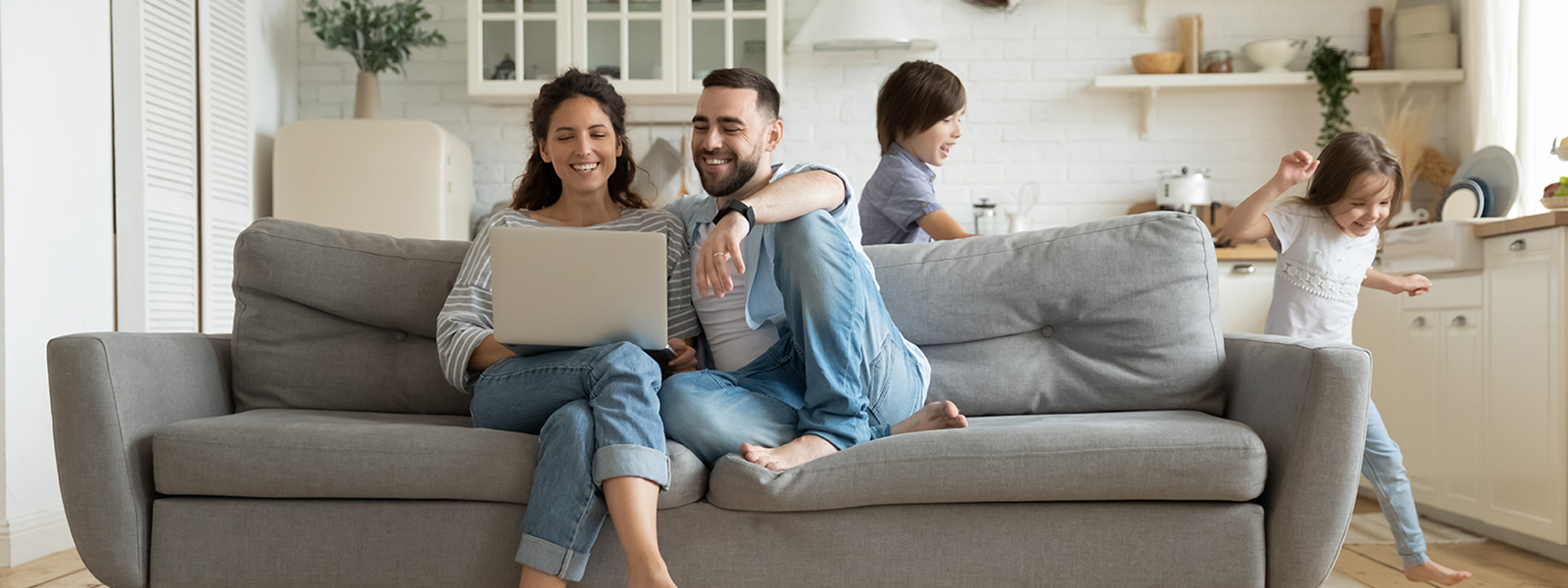 a family, with the parents looking at a laptop on the couch and kids playing