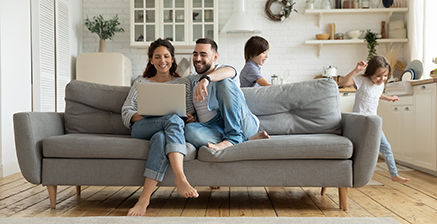 Parents on couch with a laptop and kids playing